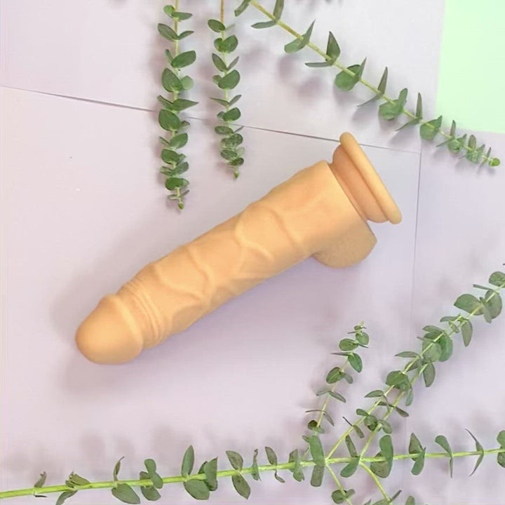 Video of Honey Play Box's Zion Silicone rotating 5.5 inch dildo rotating on a purple background with plants in the background.